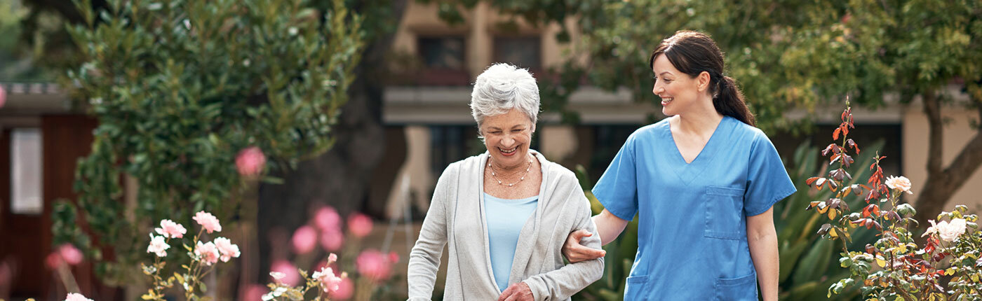 elderly white woman walking with young nurse outside